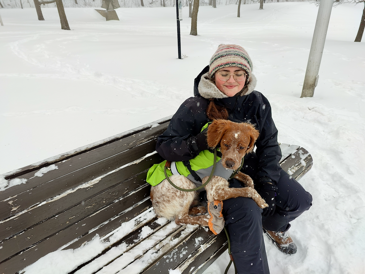 Snow-covered Gersande and Pippin sitting on a bench together, enjoying the snowy landscape.